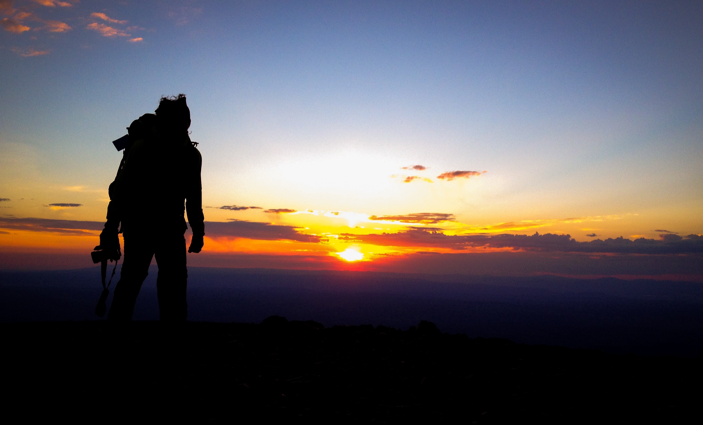 Ethan Parrish with a camera at sunset on a mountain summit